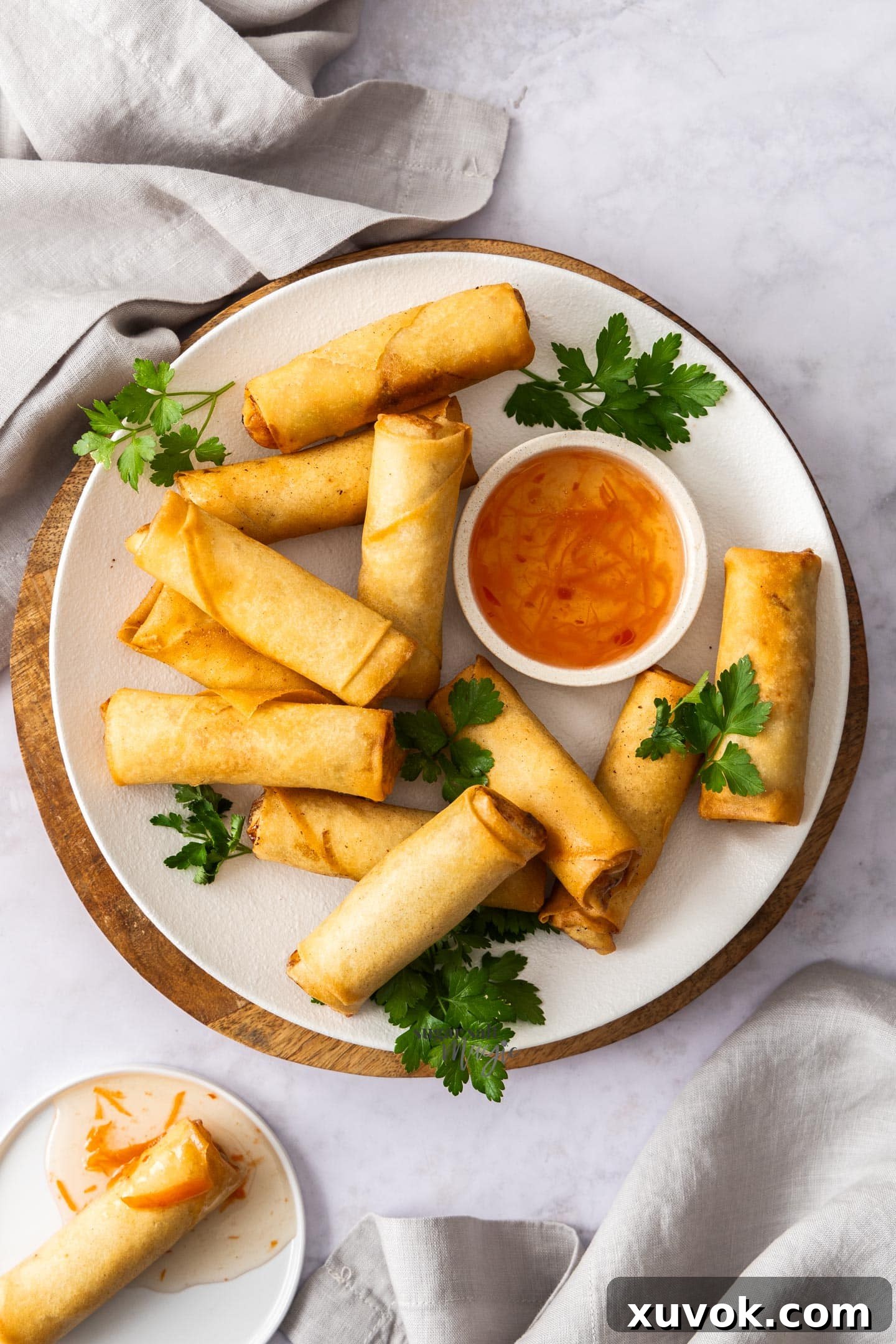 Top down view of 11 golden prawn spring rolls on a plate with a small bowl of sweet chili dipping sauce.