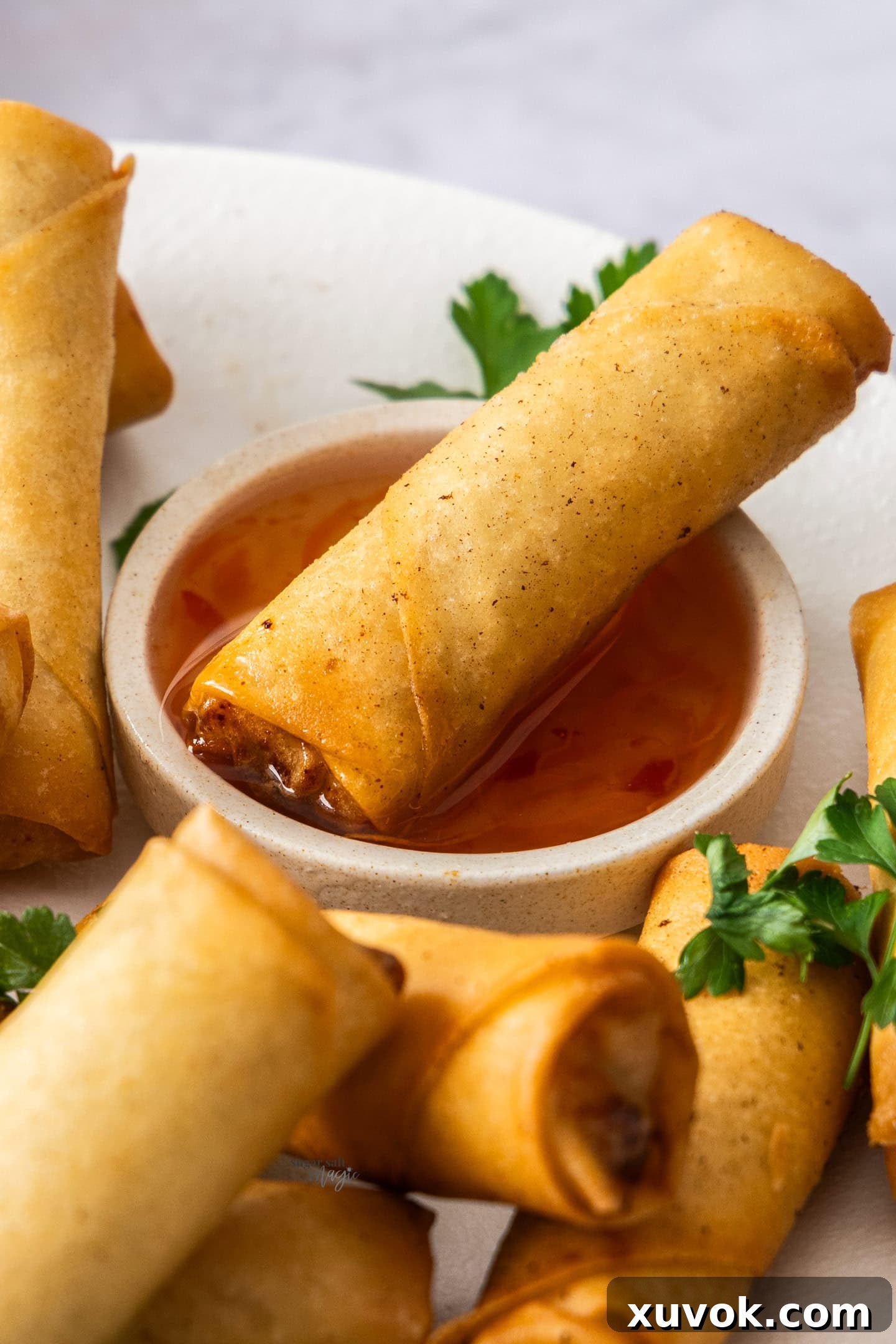 A crispy prawn spring roll dipped into a small bowl of sweet chili sauce.