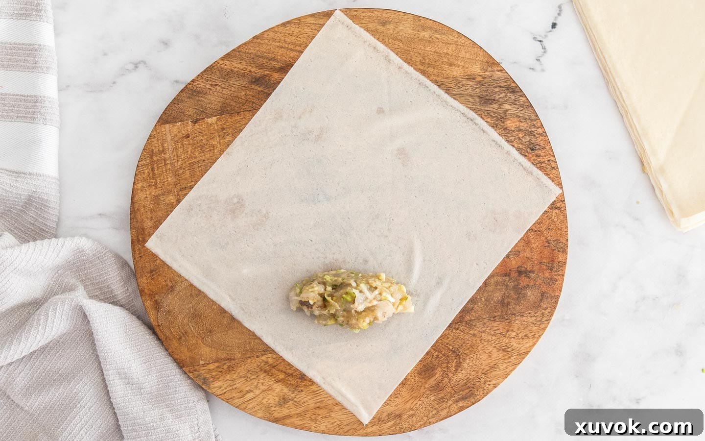 A spring roll wrapper laid out with a small portion of prawn filling in the center.