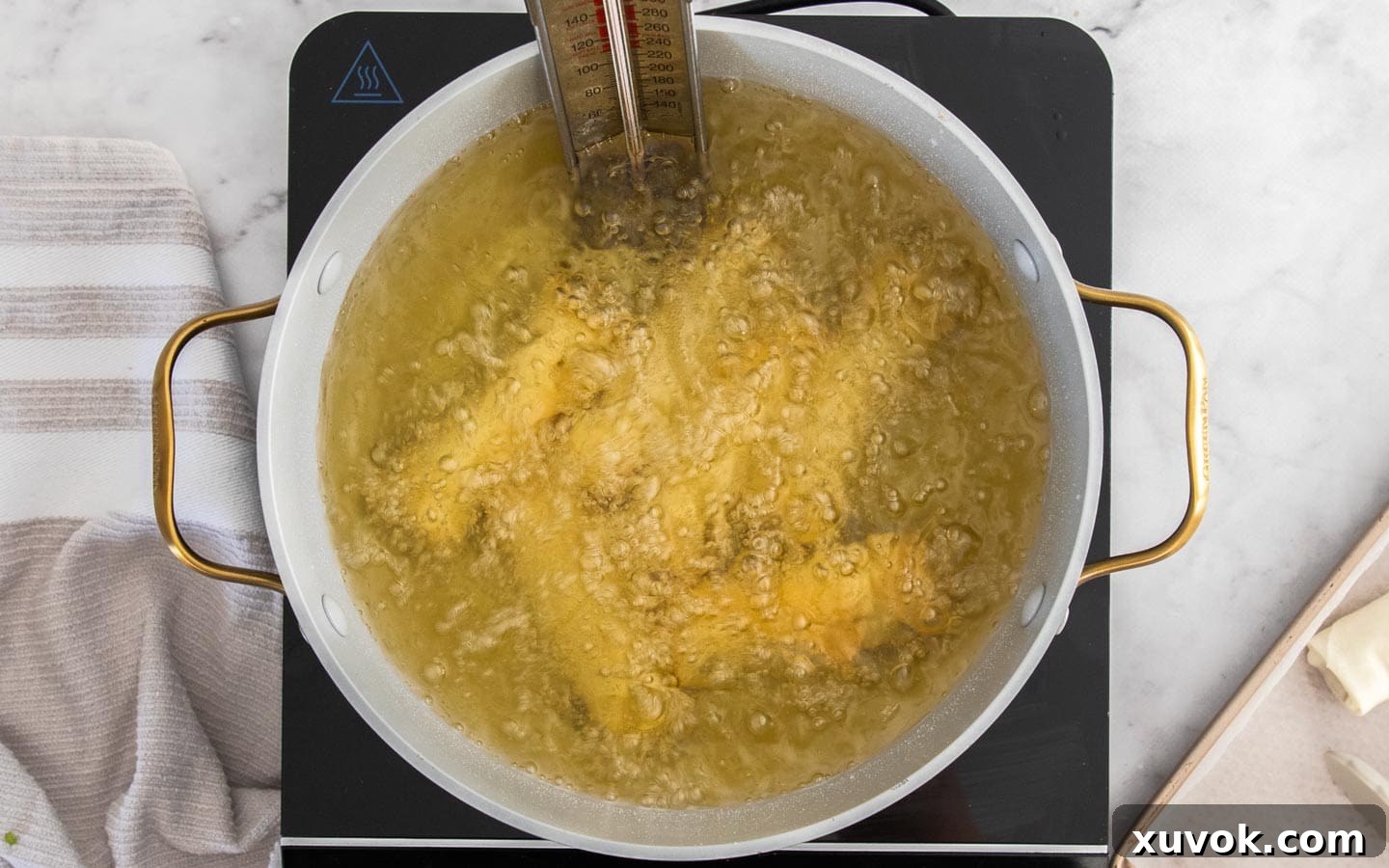 6 prawn spring rolls deep frying in a pan of hot oil, bubbling and turning golden.