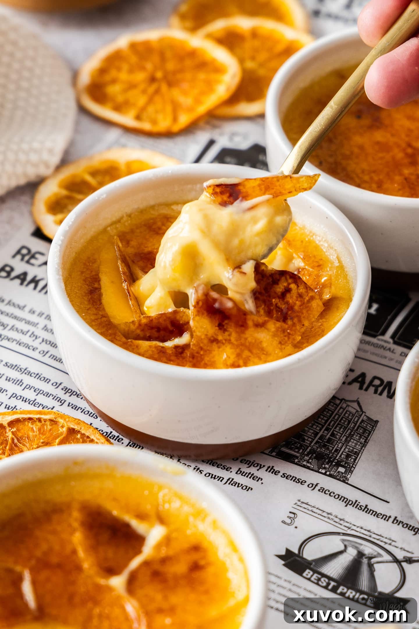 A spoon breaking through the caramelized sugar top of an orange creme brulee, revealing the creamy custard beneath.
