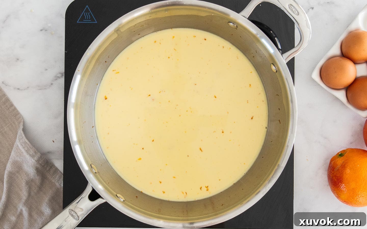 Heavy cream being poured into a saucepan containing orange-infused sugar, ready for heating and steeping.