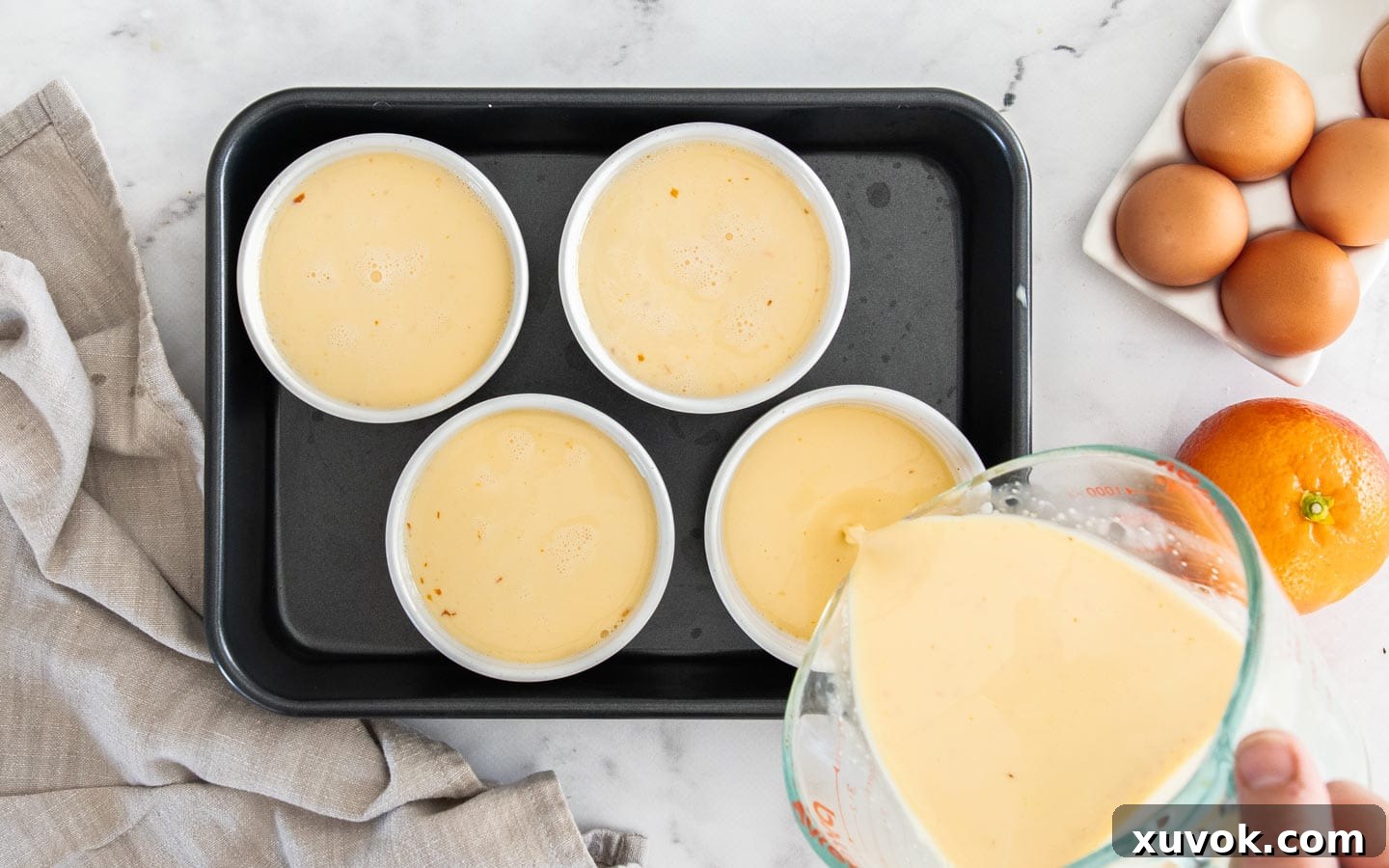 The smooth orange custard mixture being carefully poured from a jug into individual ramekins.