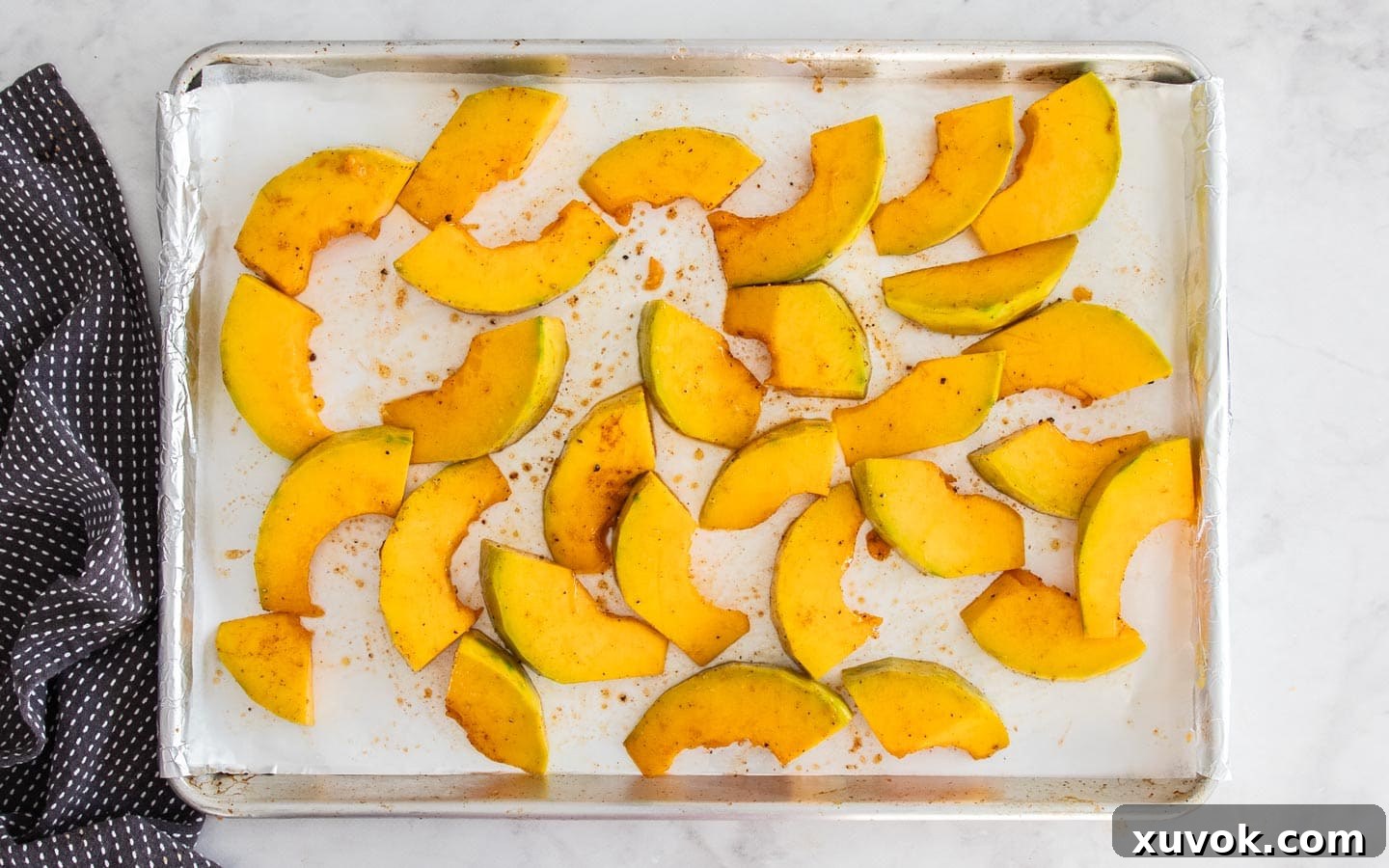 Raw pumpkin chunks tossed with oil and seasonings on a baking sheet, ready for roasting in the oven.