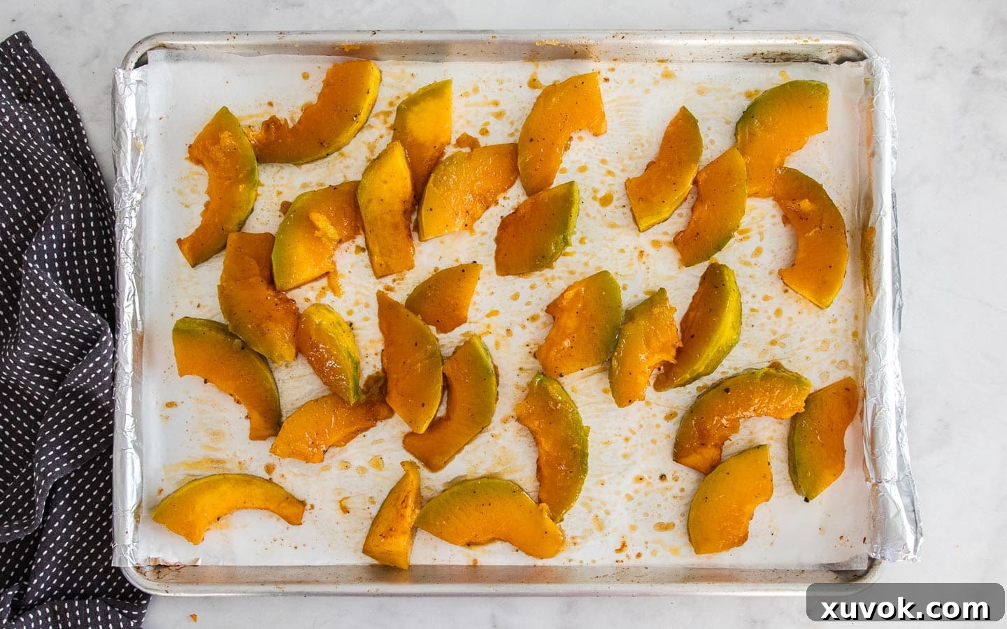 Pumpkin pieces halfway through baking, showing slight caramelization on the edges, still on the baking sheet.