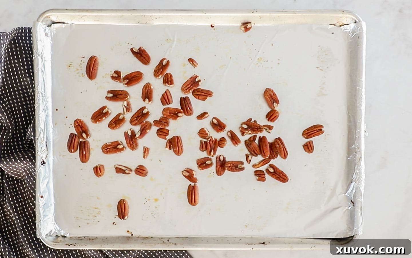 Pecan halves spread evenly on a baking tray, ready for toasting to enhance their nutty flavor.