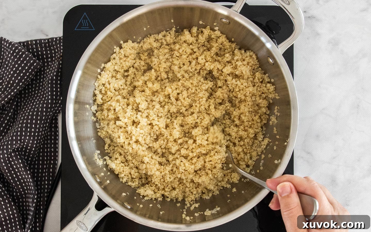 Fluffy, cooked quinoa being gently fluffed with a fork in a saucepan, ready for assembly into the salad.