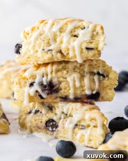 A stack of 3 blueberry and lemon scones with glaze drizzling down the sides.