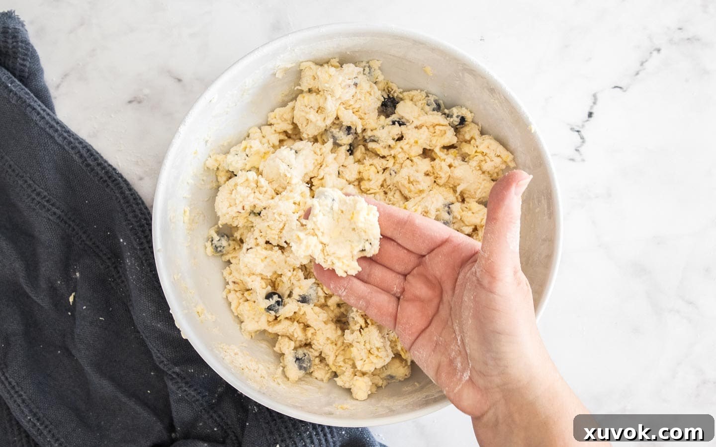 A hand holding a piece of the sticky scone dough to show the texture with blueberries.