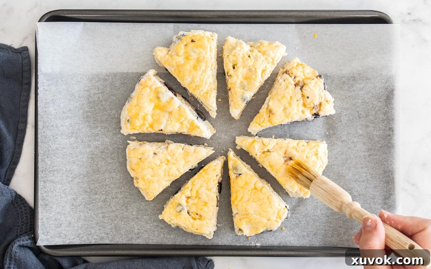 8 wedges of scone dough arranged on a baking tray, being brushed with an egg wash before baking.