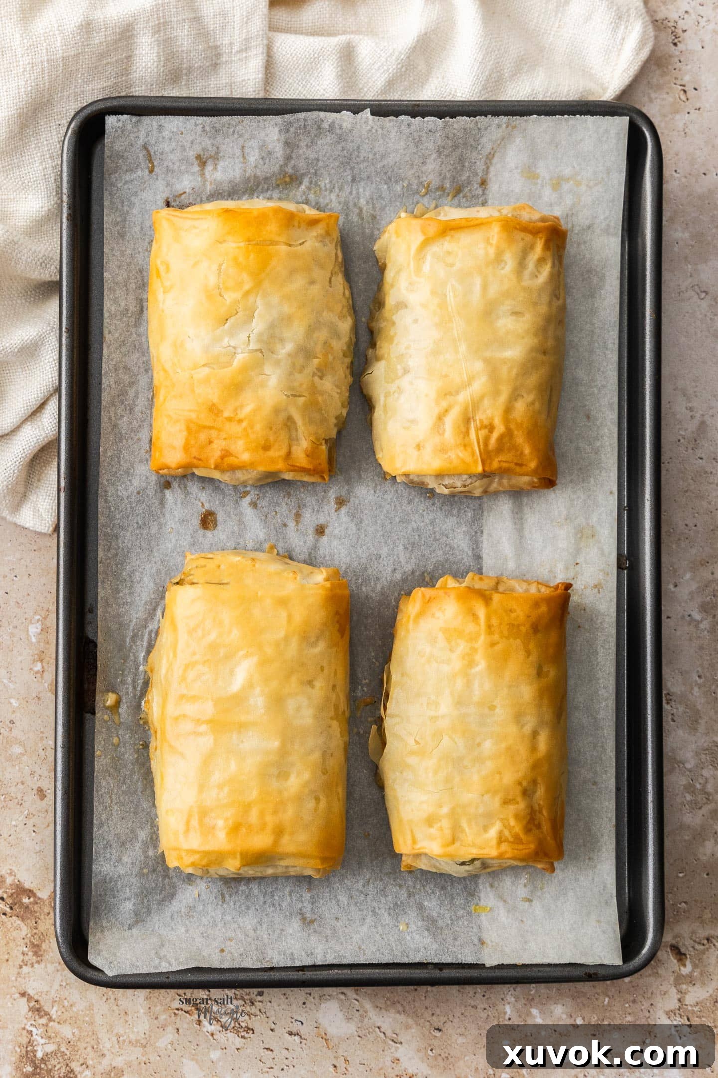 Four golden-brown chicken filo parcels, filled with creamy chicken and mushrooms, arranged neatly on a baking sheet, ready to be served.