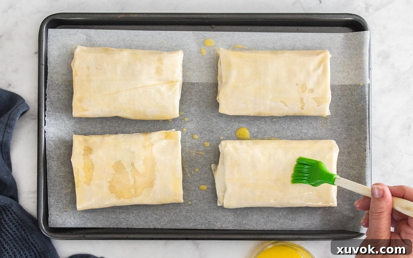 Filo parcels arranged on a baking tray, being brushed with melted butter before going into the oven for baking.