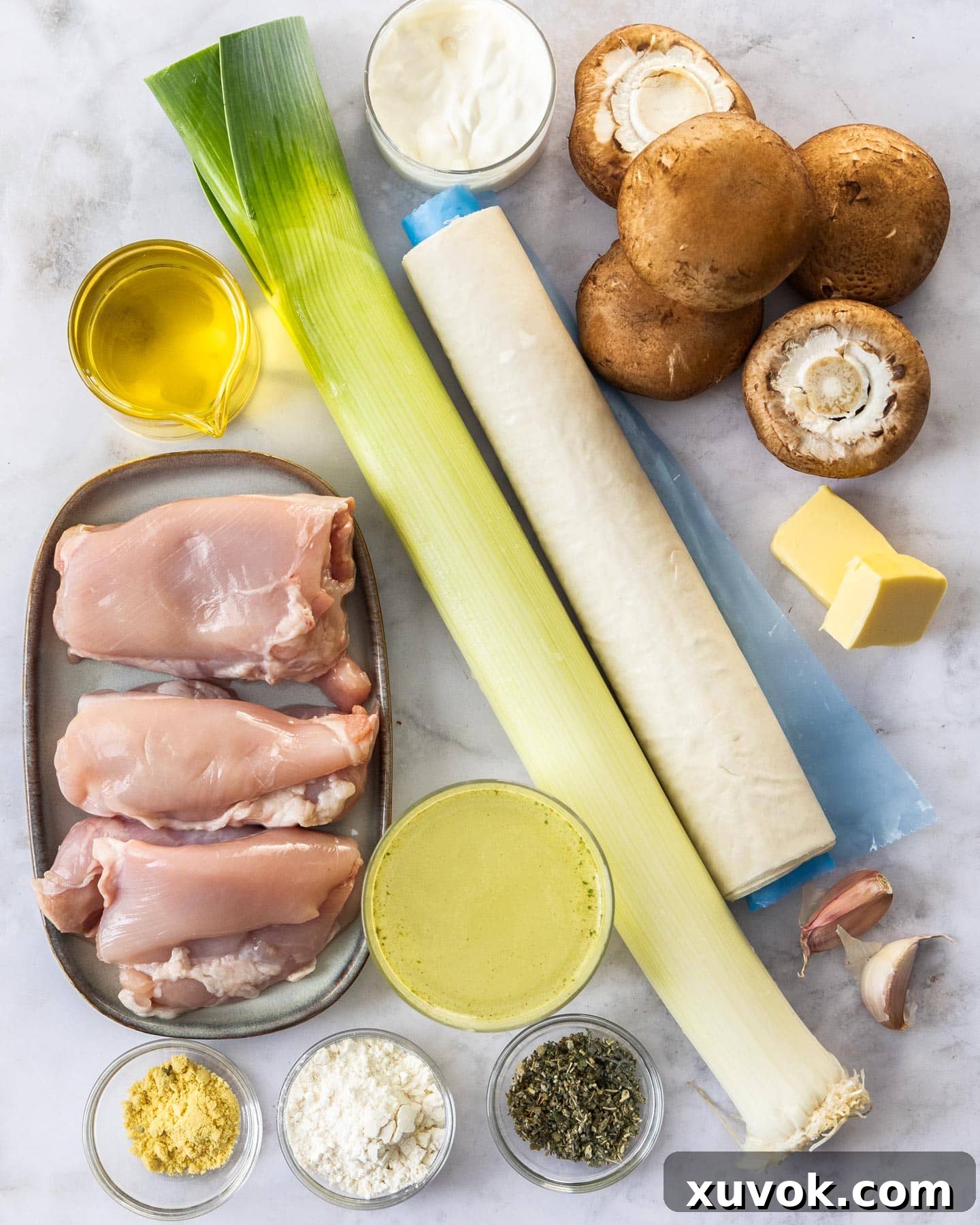 A selection of fresh ingredients including chicken, mushrooms, leek, and spices laid out on a marble surface, ready for preparing chicken filo parcels.