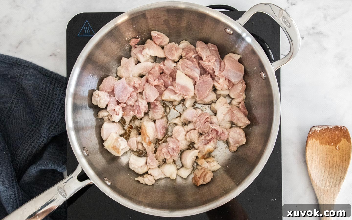 Cubed chicken thighs being cooked in a pan, achieving a golden-brown sear, as the first step in preparing the filo parcel filling.