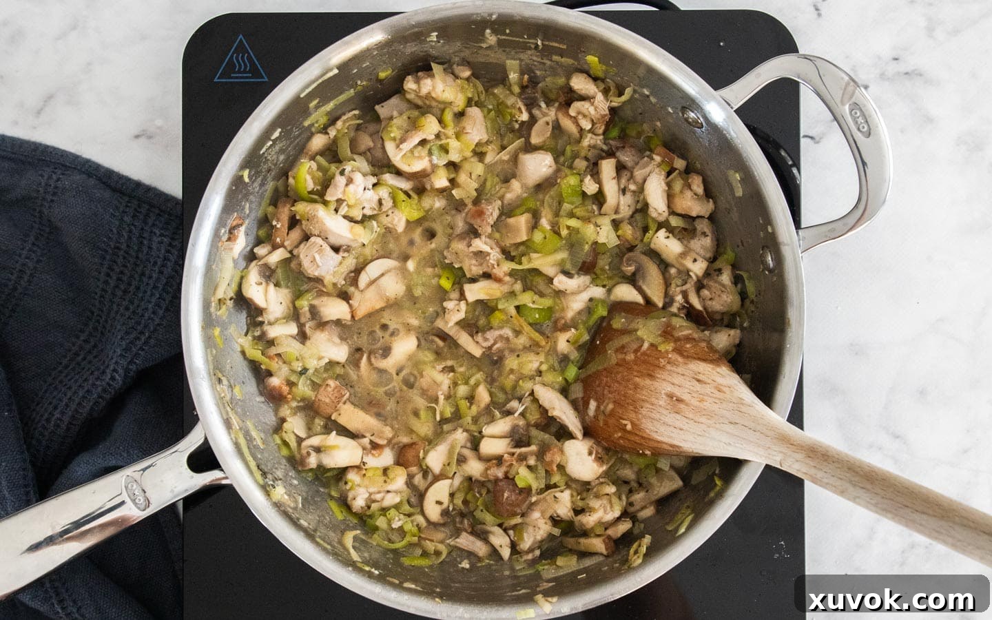 Chicken, mushrooms, and leeks simmering in a pan with chicken stock and spices, creating a rich and aromatic gravy.