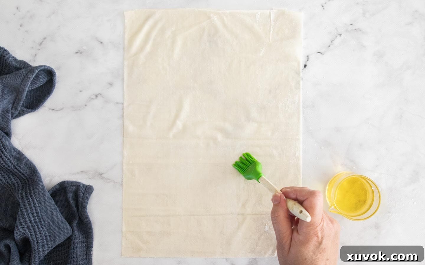 A pastry brush applies a thin layer of oil to sheets of delicate filo pastry, preparing them for wrapping the chicken filling.