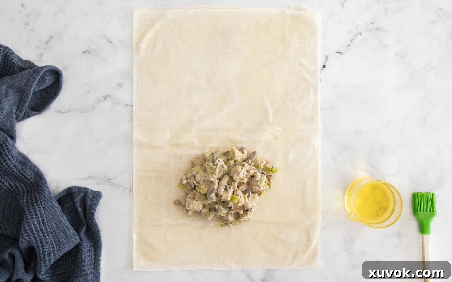 A quarter of the creamy chicken filling is carefully placed on one end of the filo pastry sheets, ready for folding.