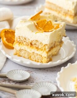 A slice of orange tiramisu on a dessert plate with ceramic spoons in front.