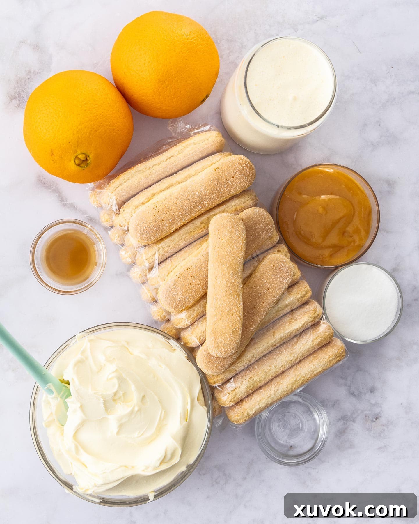 A flat lay of all the fresh and packaged ingredients laid out on a marble surface, ready for making orange tiramisu.