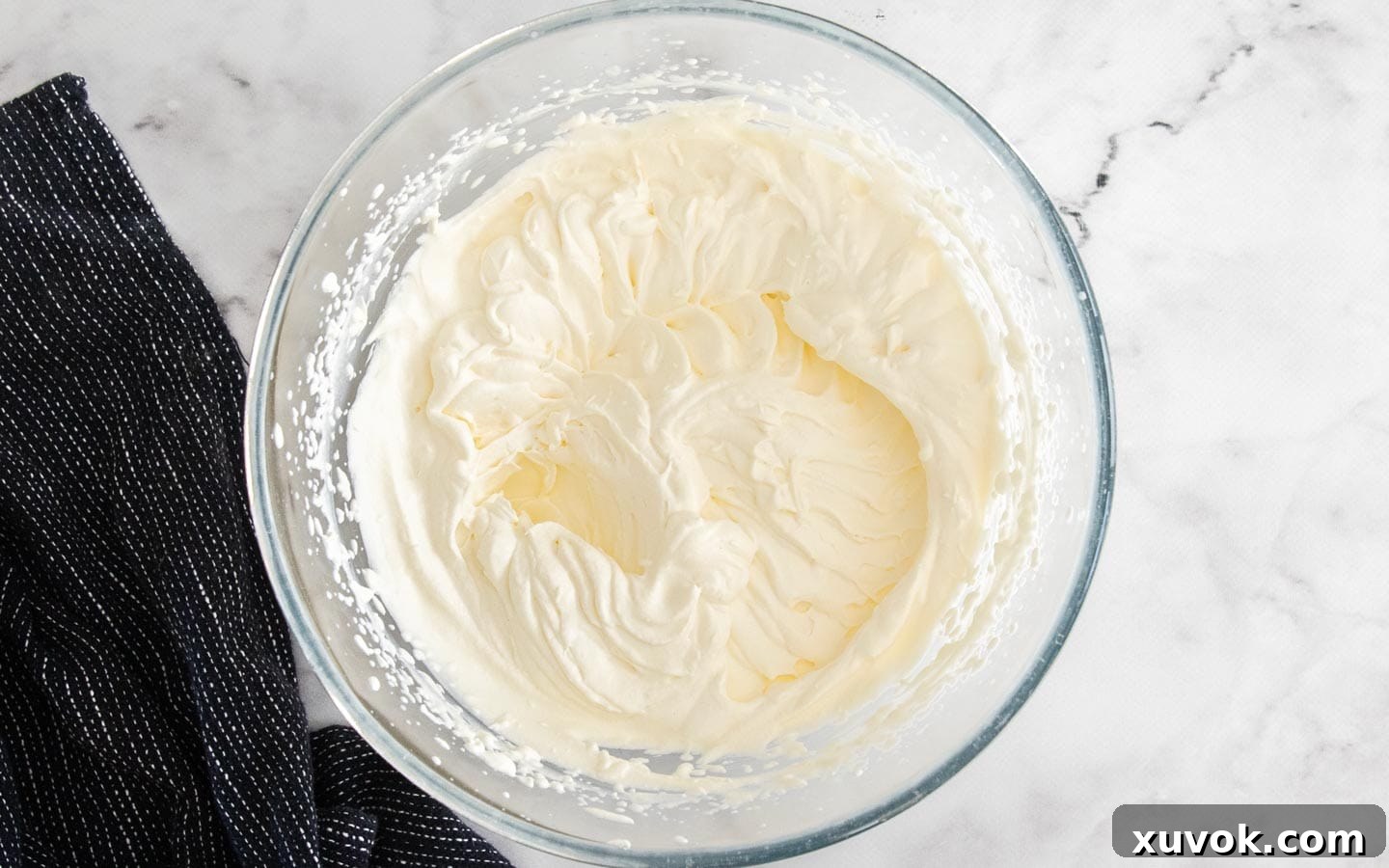 A bowl filled with perfectly whipped cream, showing soft peaks, ready to be folded into the mascarpone mixture.