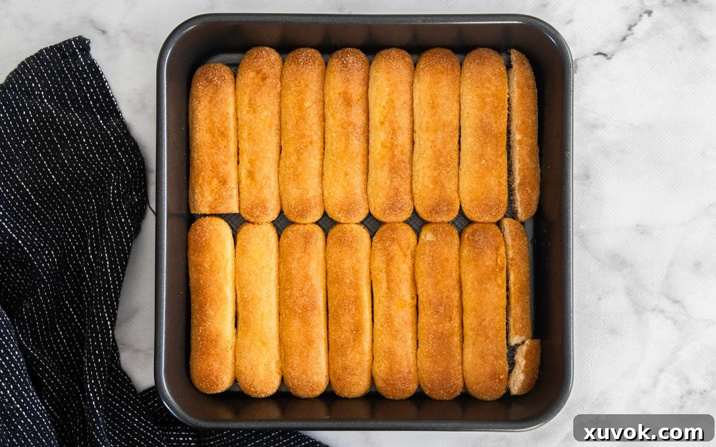 The first layer of orange juice-soaked sponge fingers neatly arranged side-by-side in a square baking tray.