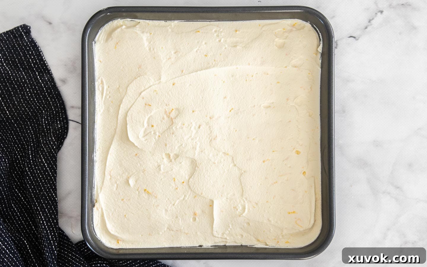 A thick, smooth layer of orange-infused mascarpone cream spread evenly over the soaked Savoiardi biscuits in a baking dish.