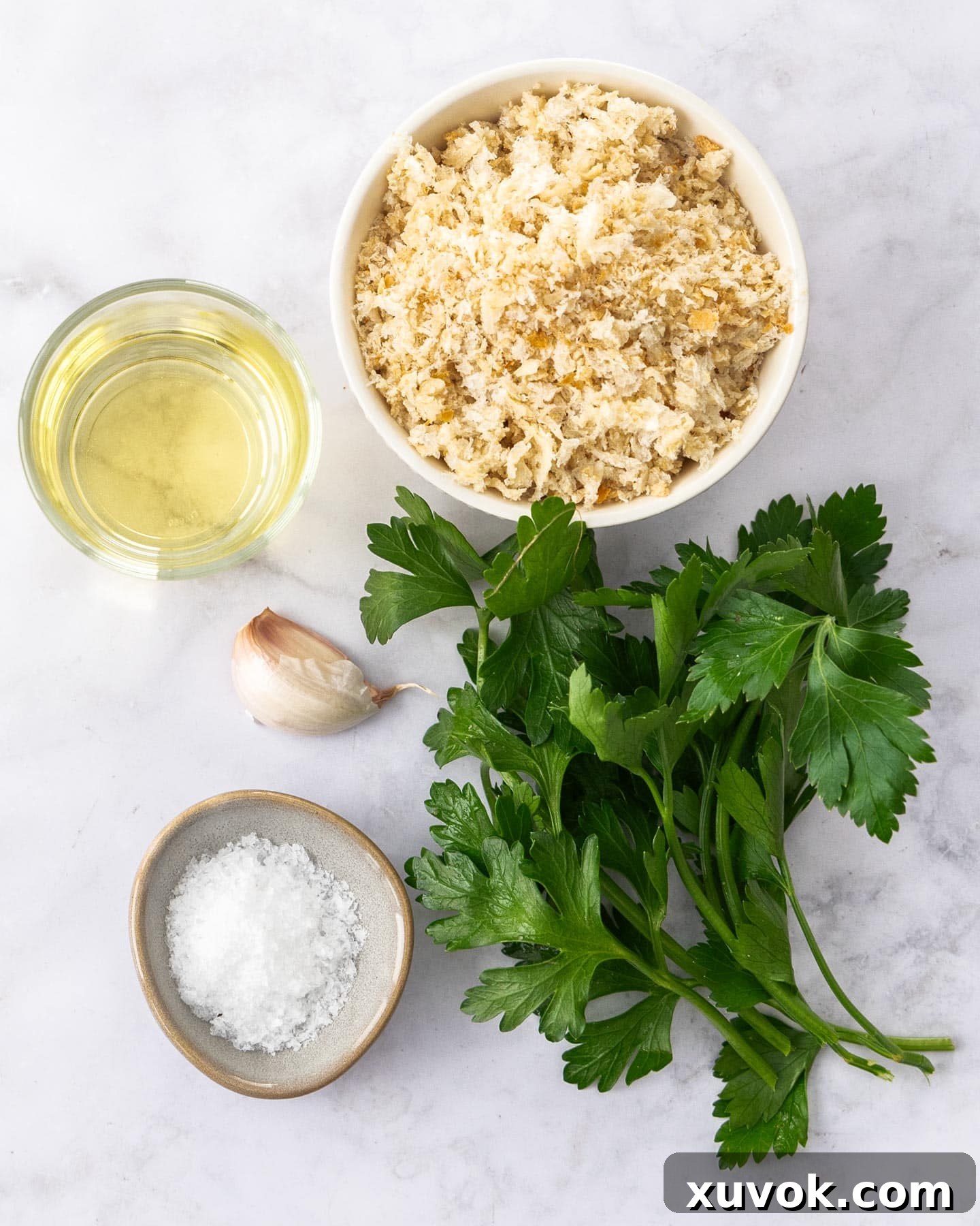 Fresh ingredients for pangrattato laid out on a rustic wooden surface: stale bread slices, whole garlic cloves, a bottle of olive oil, and a bunch of fresh parsley.
