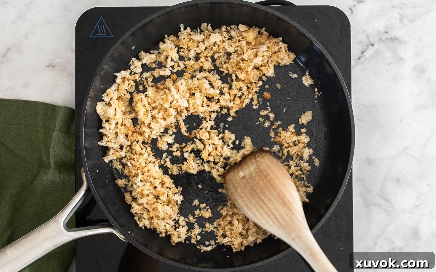 Cooking homemade breadcrumbs with minced garlic and olive oil in a hot frying pan, actively stirring them to ensure even browning.