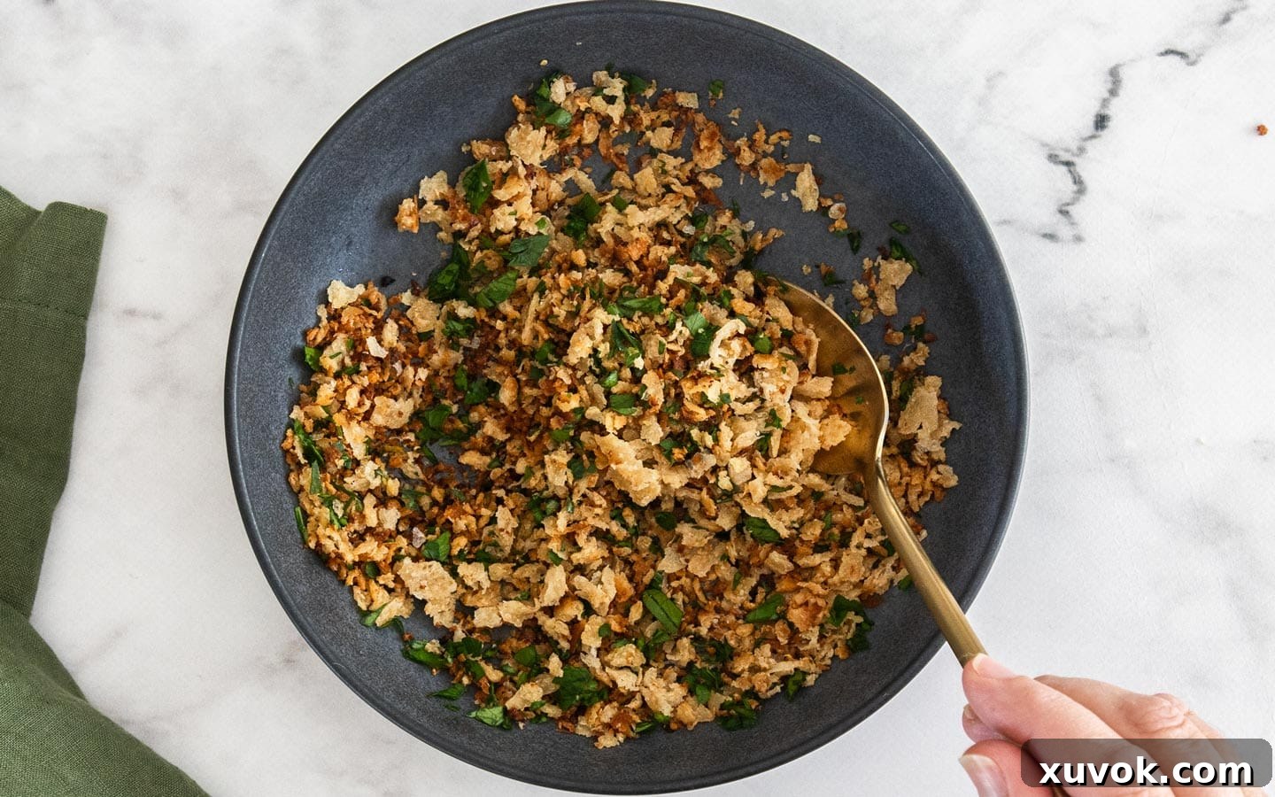 Finely chopped fresh parsley being gently stirred into a bowl of perfectly golden-brown toasted pangrattato, adding a burst of vibrant color.