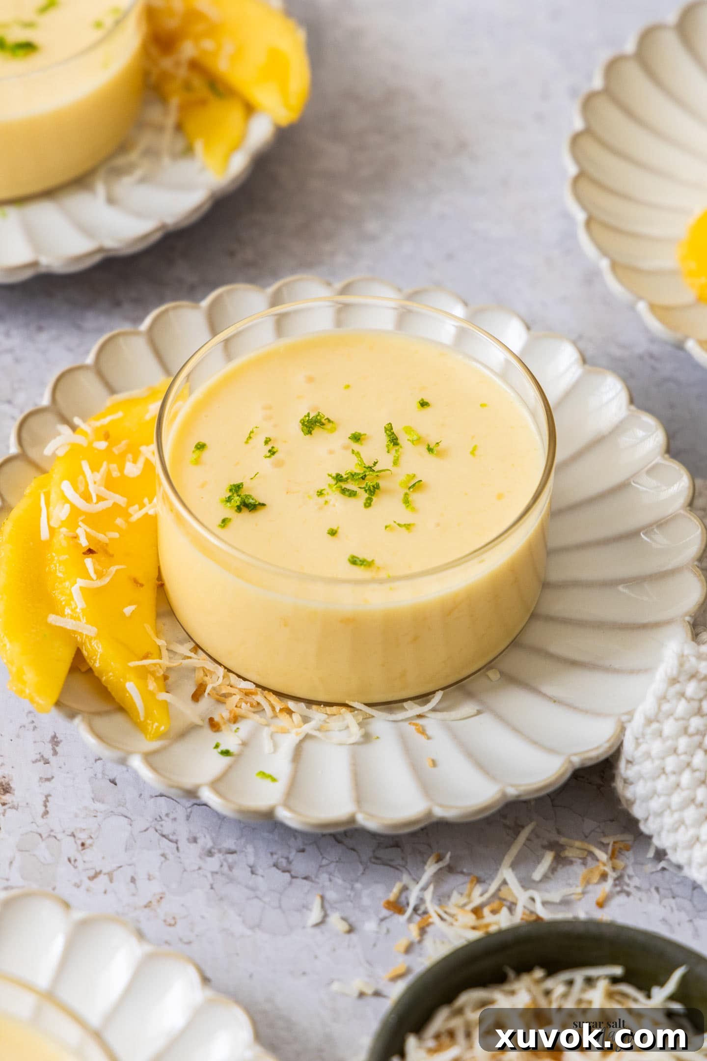 A glass ramekin filled with mango panna cotta, ready to eat, topped with a small mango slice and mint.