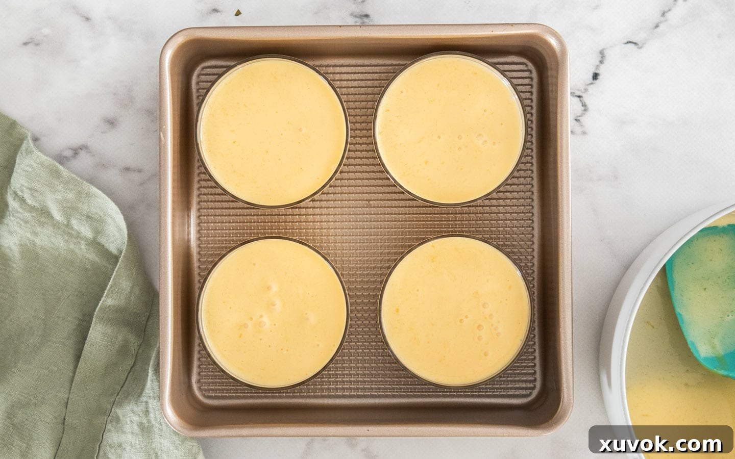 Top down view of 4 glass ramekins filled with mango panna cotta, freshly poured and ready to chill.