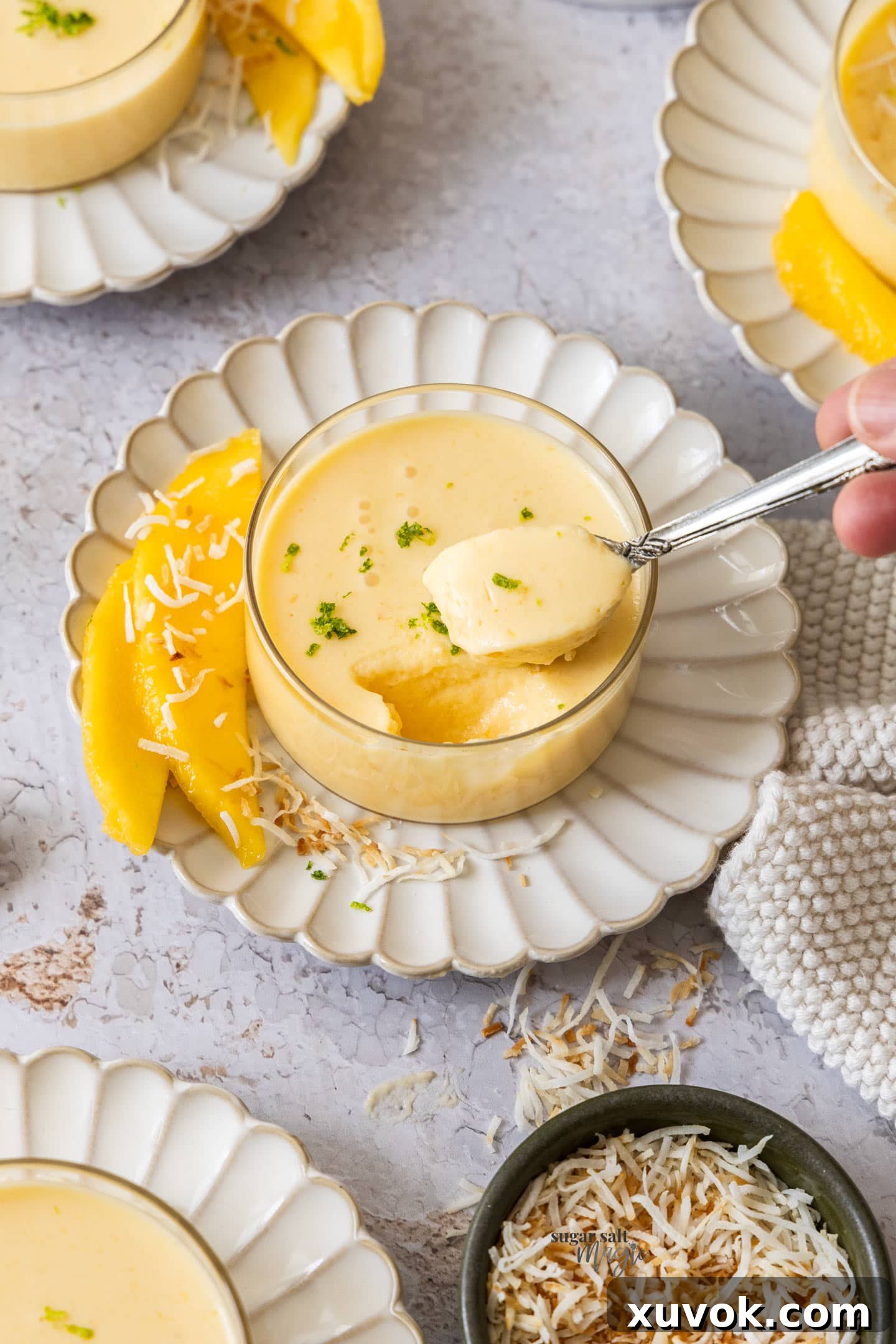 A spoon taking a scoop of mango panna cotta out of a glass dish, showing its creamy texture.