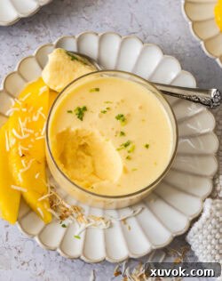 Top down view of mango panna cotta in a glass dish with a scoop taken out, garnished with mint.