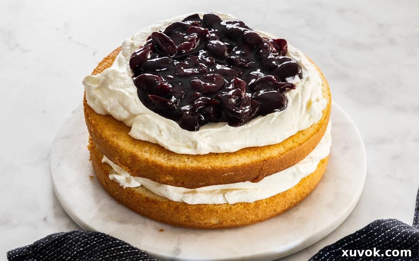 Two layers of white forest cake assembled with cream and cherry sauce, ready for the final layer.