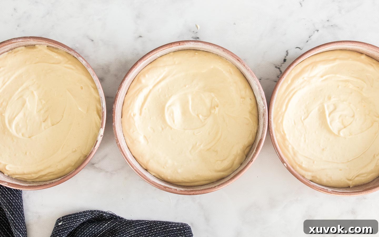 Three cake pans filled with white forest cake batter, ready for baking.