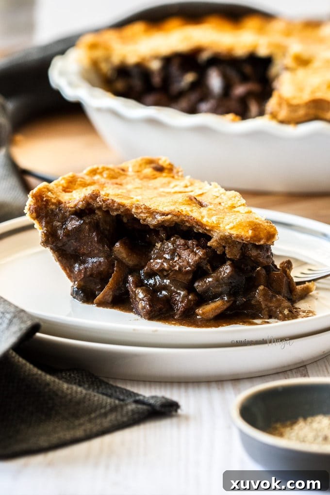 A perfectly portioned slice of steak pie on a white plate with a fork next to it, inviting you to take a bite.