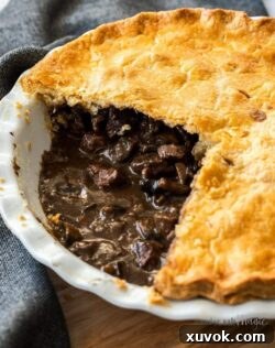 Closeup of the in meat filling in a pie in a white pie dish. It sits on a wooden board.