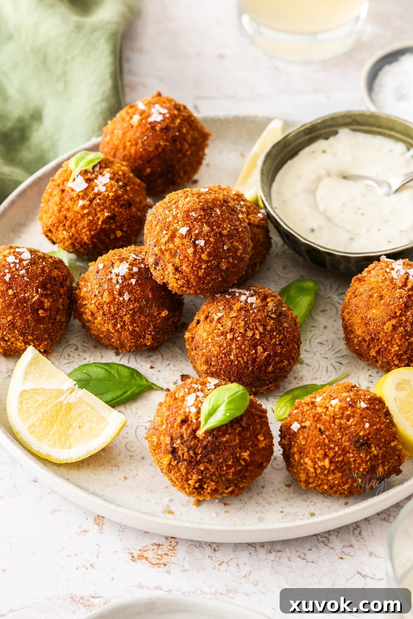A platter of golden-fried Tomato Arancini balls, garnished with lemon wedges and a small bowl of creamy aioli. One arancino is cut in half, revealing a melted mozzarella core.