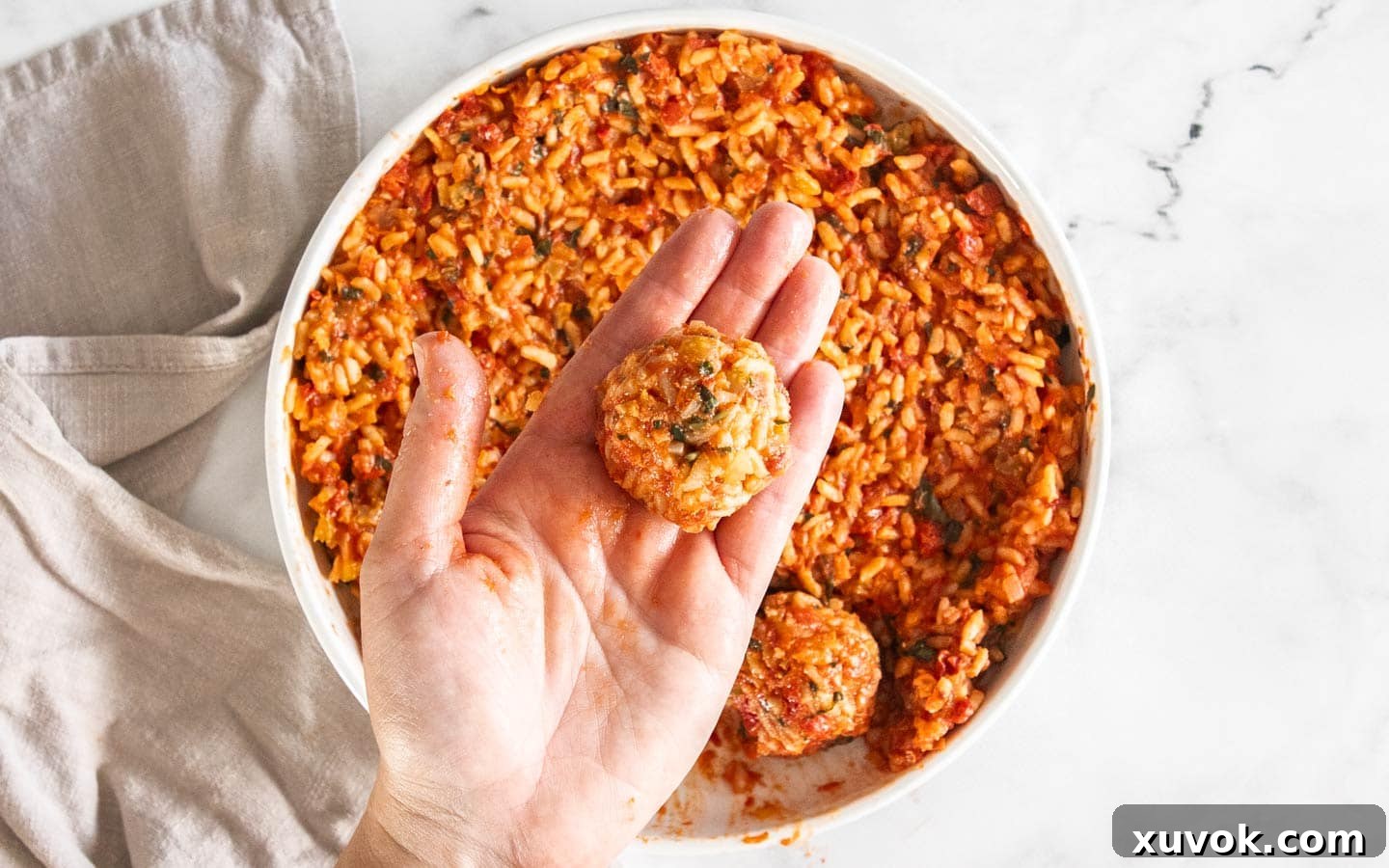 A hand holding a perfectly rolled ball of tomato risotto rice, ready for breading.