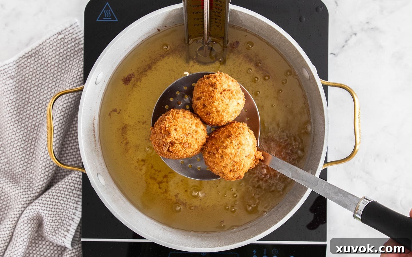 A slotted spoon lifting three golden-fried arancini out of the hot oil.