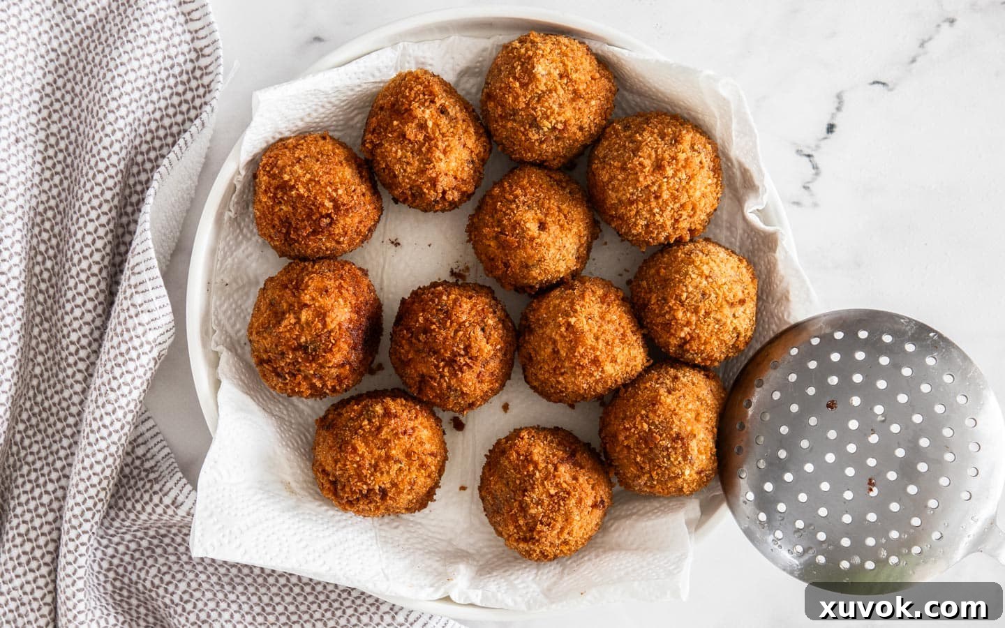 A dozen freshly fried arancini draining on a plate lined with paper towel.