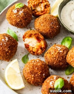 Crispy Tomato Arancini balls on a platter with lemon wedges and one cut in half revealing molten cheese.