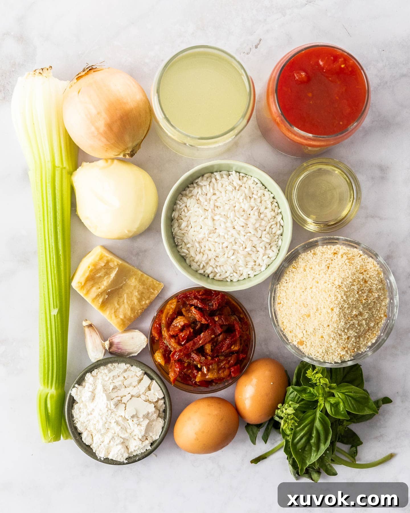 Various fresh ingredients for making tomato arancini laid out on a marble surface, including canned tomatoes, rice, basil, and cheese.