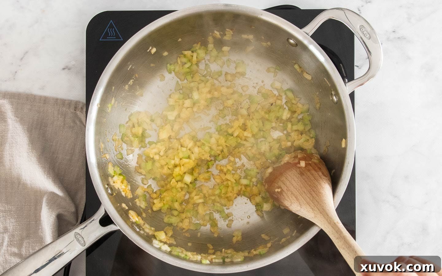 Finely chopped onion, celery, and garlic cooking in a stainless steel pan.