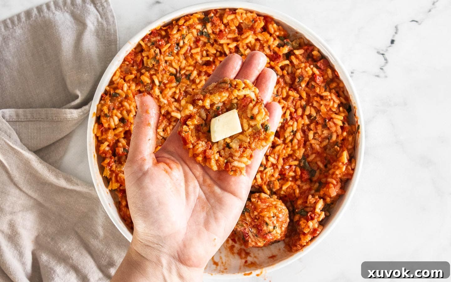 A hand holding a portion of cold tomato risotto with a cube of mozzarella cheese placed on top.