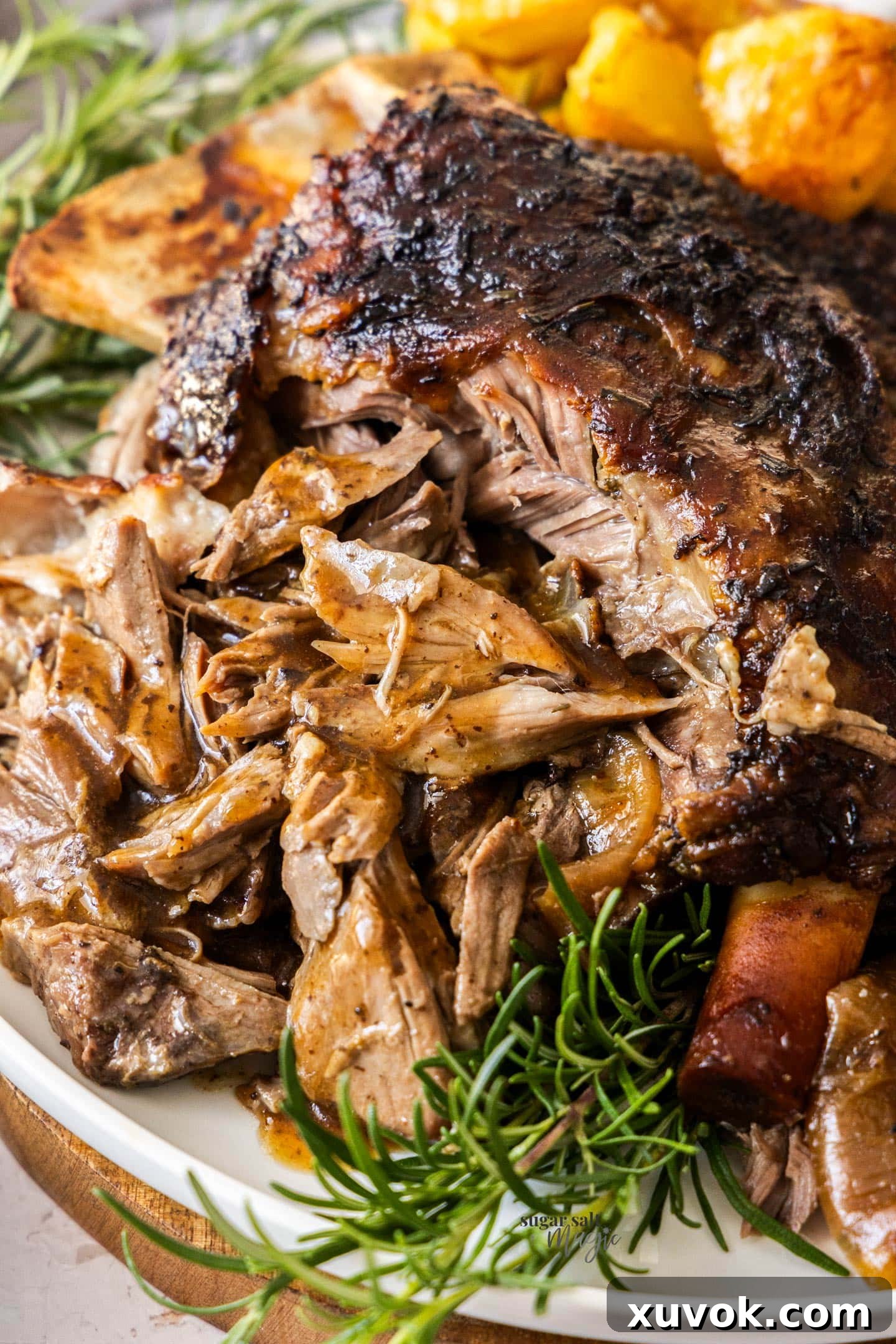 Succulent, gravy-soaked slow cooked pulled lamb shoulder with roasted potatoes in the background, ready to be served.