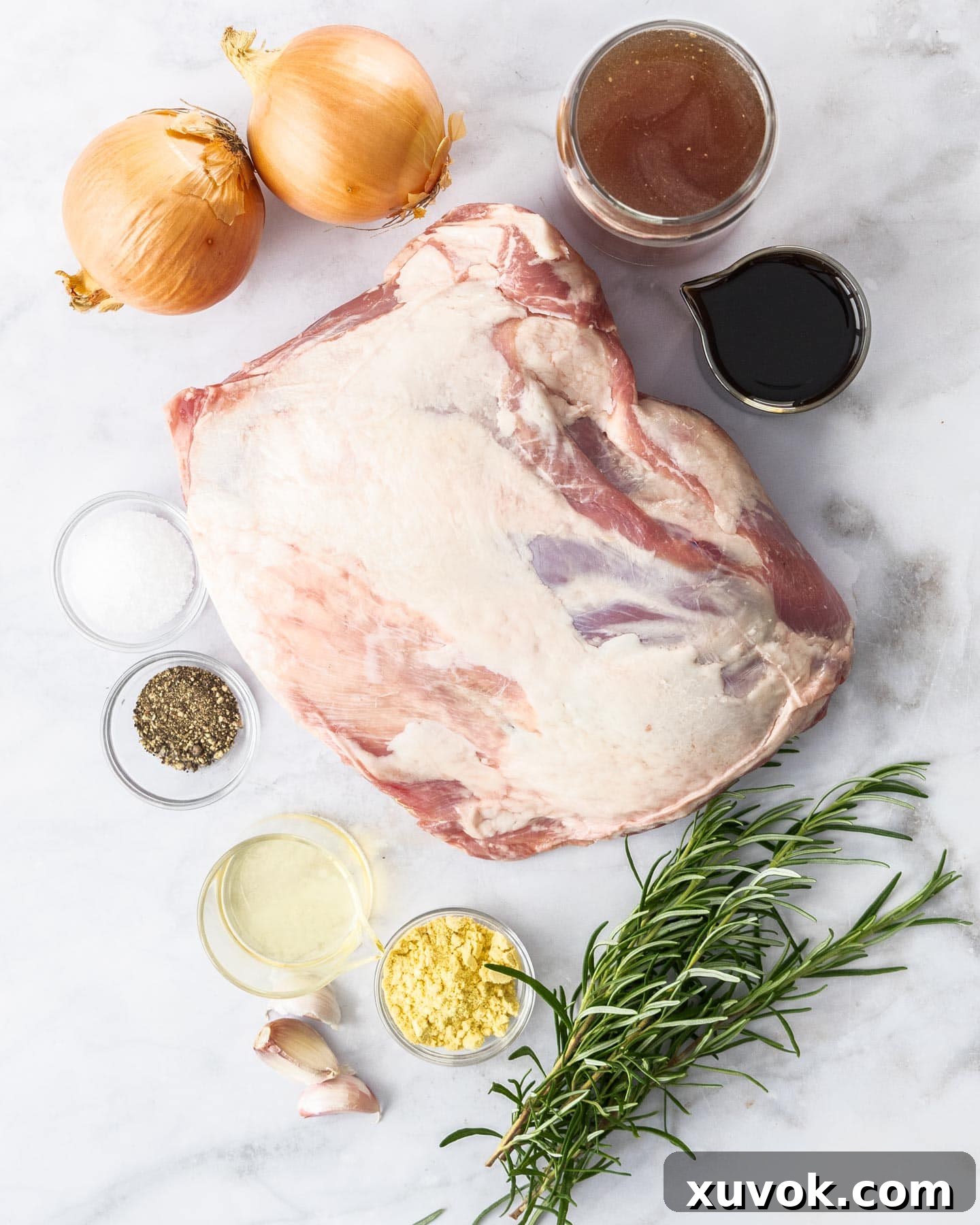Fresh ingredients laid out on a marble surface, including bone-in lamb shoulder, rosemary, garlic, onions, and spices for slow cooking.