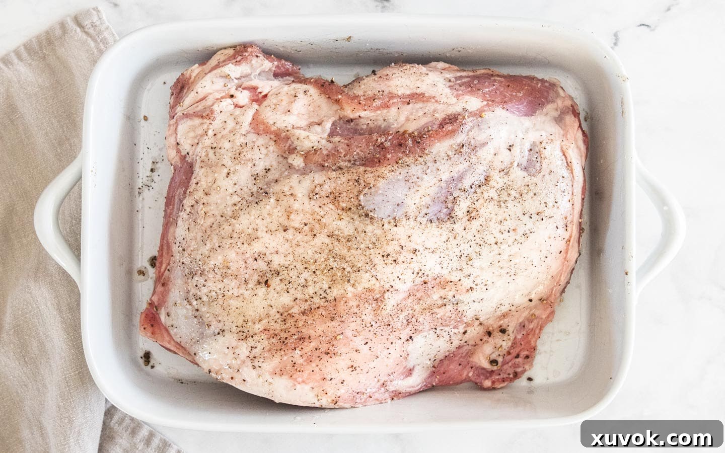 Bone-in lamb shoulder seasoned with salt, pepper, and oil, resting in a baking dish before brining.