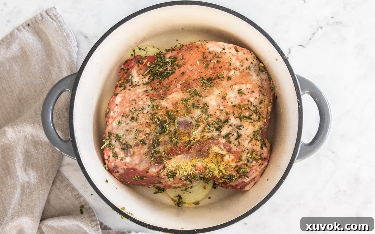 Lamb shoulder seasoned with herbs and spices, resting on a bed of sliced onions in a Dutch oven, ready for slow roasting.