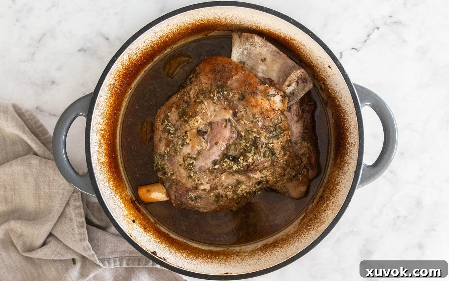 Slow cooked lamb shoulder after 2.5 hours of roasting, surrounded by rich pan juices in a Dutch oven.